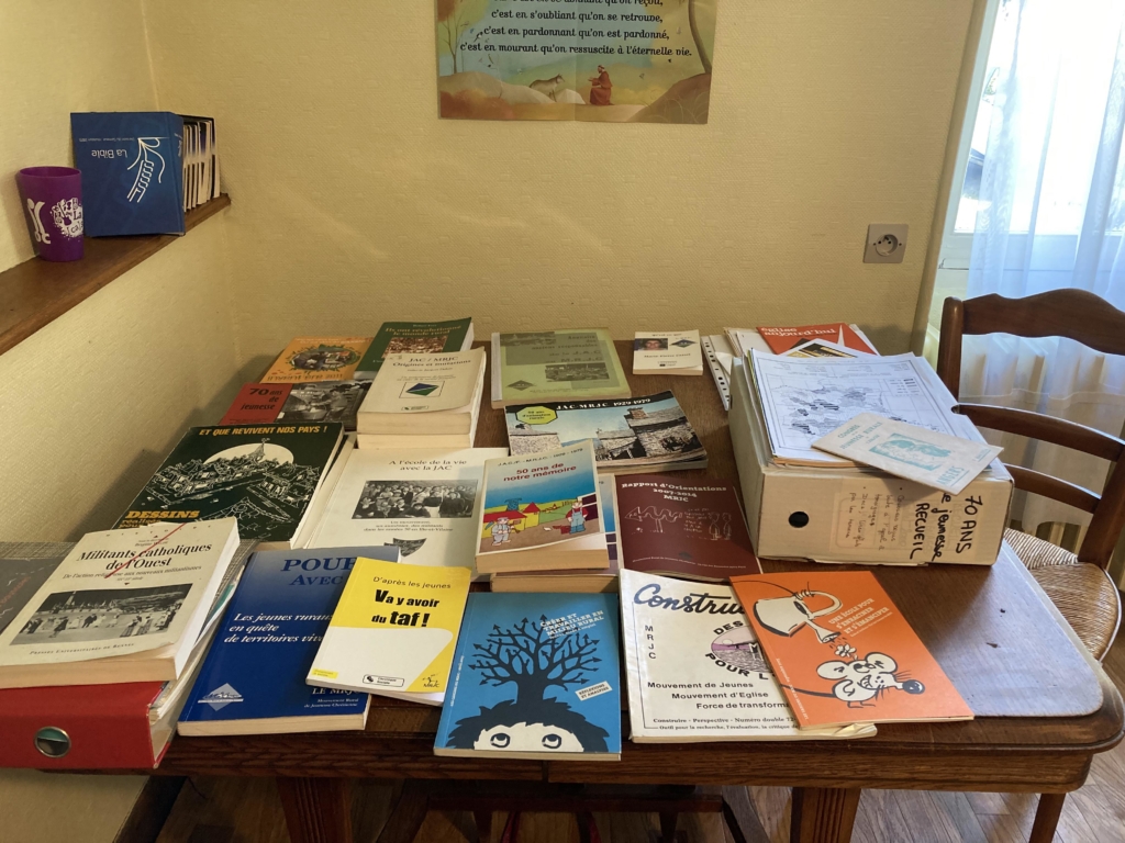 Table en bois avec une vingtaine de livres et de documents dessus traitant de l'histoire du MRJC